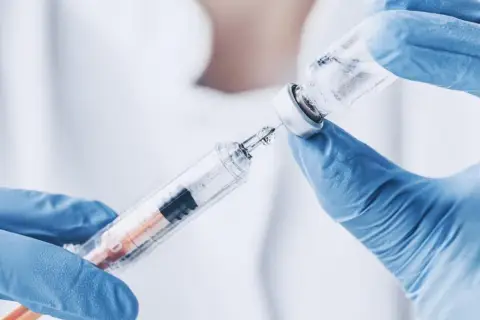Ręce w niebieskich rękawiczkach pobierają płyn z fiolki do strzykawki. To może być propofol, środek znieczulający.