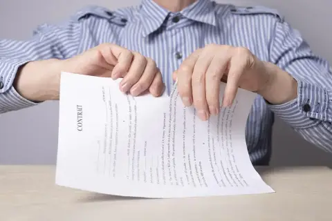 Ręce drą umowę. Bank wypowiedział umowę kredytu, co symbolizuje podarcie dokumentu.
