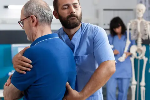 Fizjoterapeuta pomaga pacjentowi z bólem pleców i mięśni. W tle szkielet i pielęgniarka.