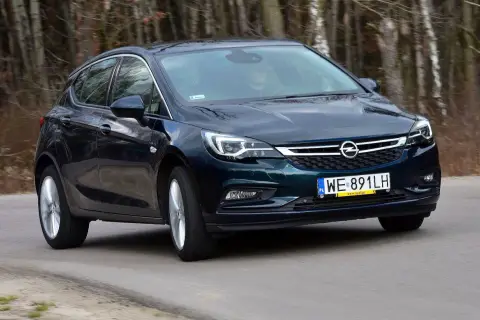 Ciemnozielony Opel Astra K 1.4 Turbo jedzie po drodze wśród drzew.