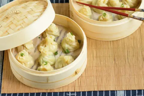 Parujące pierożki z ciasta do wontonów w bambusowych parownikach, ozdobione szczypiorkiem.