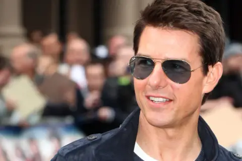 Tom Cruise w okularach przeciwsłonecznych, uśmiechnięty, na tle tłumu. Wygląda jakby właśnie świętował swoje urodziny, kiedy urodził się Tom Cruise.