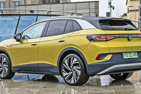 Żółty VW ID.4 z czarnym dachem i felgami stoi na mokrym chodniku.