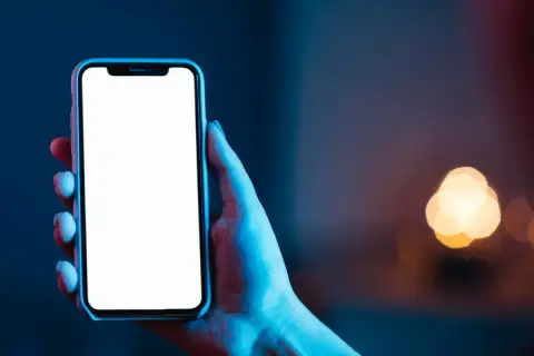 Dłoń trzyma smartfon z pustym ekranem **AMOLED**, otoczony niebieskim i czerwonym światłem.