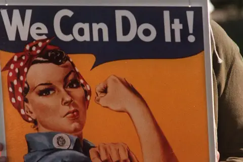En person håller upp en affisch med Rosie the Riveter och texten "We Can Do It!". En symbol för styrka och beslutsamhet.