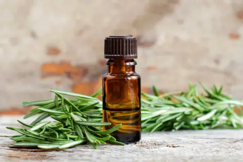 Aceite esencial de romero para el pelo, con ramitas frescas de romero sobre madera rústica.