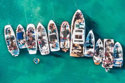 Grupa łodzi cumuje blisko siebie na turkusowej wodzie, tworząc wrażenie wodnego festiwalu. To idealny prom majorka ibiza dla miłośników słońca i zabawy na morzu.