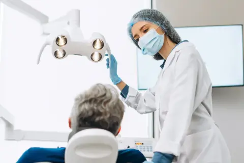 Dentystka w masce i rękawiczkach przygotowuje się do zabiegu. Pacjent siedzi na fotelu. Czy dentysta może wystawić L4?