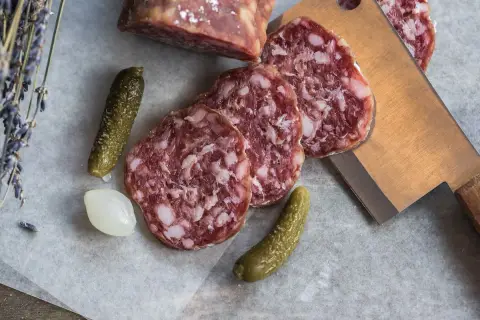 Plasterki salami z widocznym tłuszczem, ogórki konserwowe i cebulka. Salami jest z mięsa wieprzowego i wołowego.
