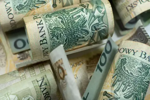 Zwijane banknoty 100 zł, czyli kosiniakowe, tworzą stos. Widoczny orzeł i napis Narodowy Bank Polski.