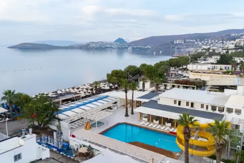 Widok na basen i plażę z leżakami. W tle morze i zabudowania. Idealne miejsce na wakacje, jak sugerują petunya beach resort opinie.