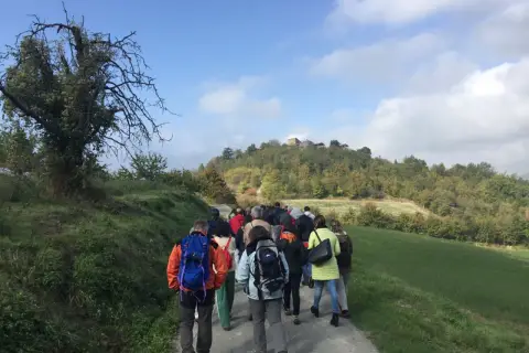 Gruppo di escursionisti sul sentiero delle fontane, con colline boscose e un borgo in cima.