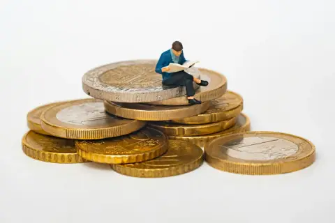 Figurka siedząca na stosie monet euro, czytająca gazetę. Symbolizuje eurocent pożyczki do domu.