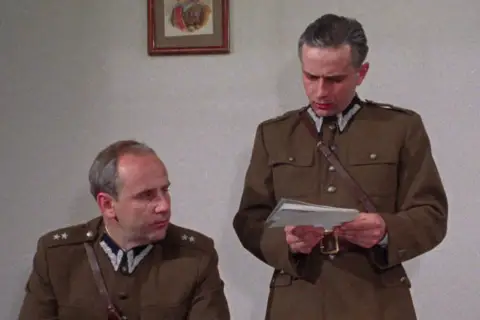 Dwóch mężczyzn w mundurach wojskowych, jeden czyta dokument. Scena z filmu "Pogranicze w ogniu obsada".