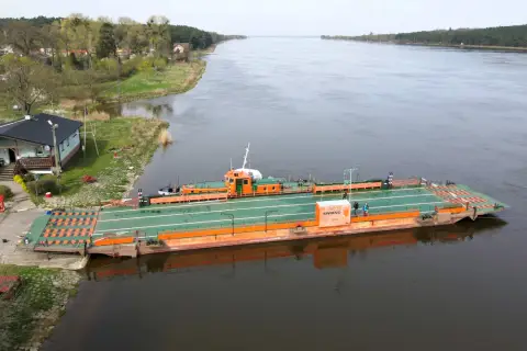 Prom "Świbno" czeka na pasażerów przy brzegu, gotowy do przeprawy przez szeroką rzekę.
