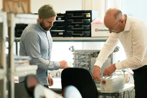Två män arbetar med elektronik. En creative director ser på när en kollega kopplar ihop komponenter.