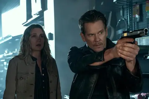 Kevin Bacon jako łowca nagród w serialu, z pistoletem w ręku, obok przerażonej kobiety.
