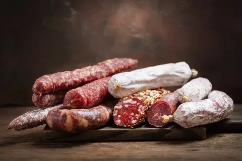 Ein Haufen verschiedener Salamisorten, von denen einige mit Gewürzen bedeckt sind. Die Frage, ob **ist schweinefleisch ungesund**, bleibt bei dieser appetitlichen Auswahl offen.