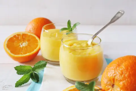 Dwa szklanki orzeźwiającego, gęstego **orange curd** z miętą i świeżymi pomarańczami.
