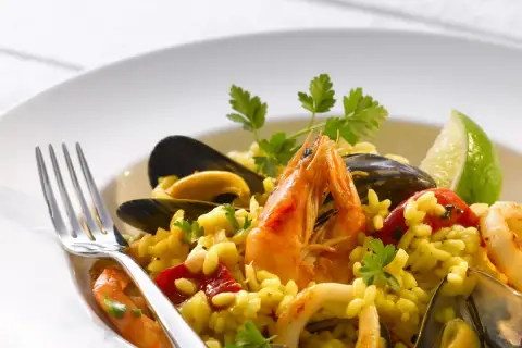 Pyszne risotto z owocami morza: krewetki, małże, kalmary i ryż, udekorowane natką pietruszki i ćwiartką limonki.