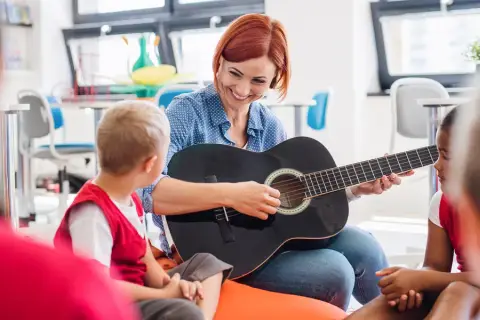 Nauczycielka gra na gitarze dla dzieci, tworząc zindywidualizowaną ścieżkę kształcenia. Przykłady takiej nauki to muzyka.