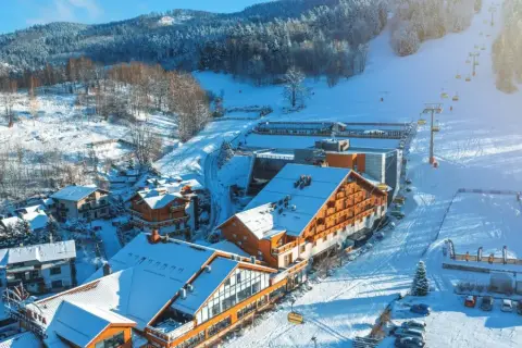 Idealne miejsce na ferie zimowe: ośnieżone góry, hotel z drewnianą elewacją i wyciąg krzesełkowy.