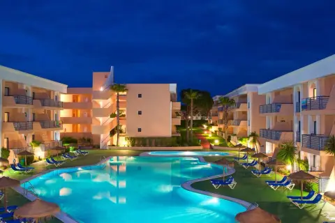 Resort con piscina iluminada y edificios de apartamentos bajo el cielo nocturno. Un lugar perfecto para disfrutar del sol Sancti Petri.