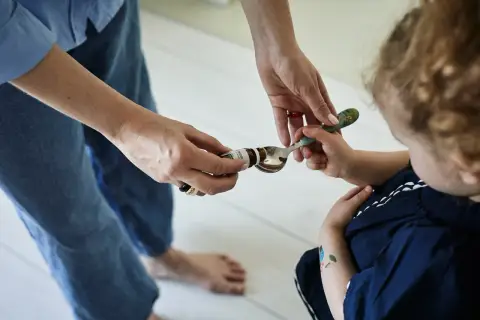 Mama podaje dziecku łyżeczkę z kroplami psychobiotyku. Dziecko z zaciekawieniem patrzy na podawany specyfik.