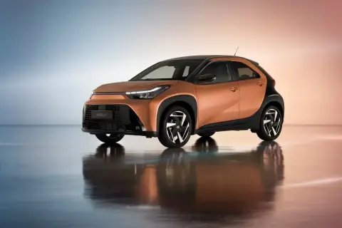 Pomarańczowy Toyota Aygo Cross z czarnymi akcentami i stylowymi felgami, odbijający się w lustrzanej podłodze.