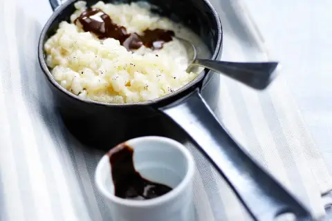 Un délicieux riz au lait au chocolat, servi dans une petite casserole noire, avec une cuillère et un ramequin de sauce chocolat.