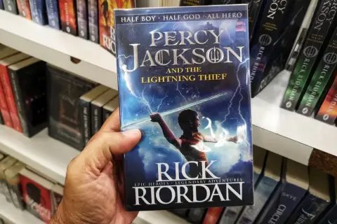 Dłoń trzyma okładkę książki "Percy Jackson i Złodziej Pioruna". Na okładce młody bohater z mieczem w ręku, otoczony błyskawicami.