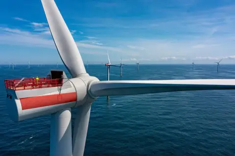 Wielka turbina wiatrowa na morzu, część projektu Baltica 2, z pracownikami na platformie. W tle widać kolejne morskie farmy wiatrowe.