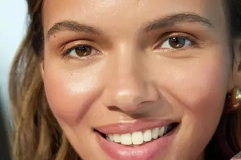 Una mujer sonríe, mostrando su piel radiante. Sostiene un producto con agua de rosas, ideal para la doble limpieza facial.
