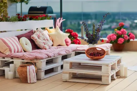 Un canapé en palette plan, confortable et coloré, orne cette terrasse avec des coussins douillets et des fleurs vives.