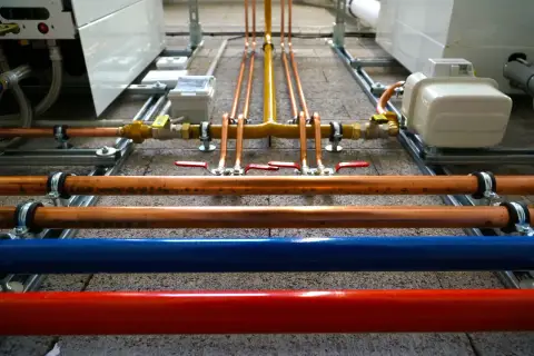 Instalacja hydrauliczna z miedzianymi rurami, zaworami i niebieską/czerwoną rurą. Ocieplenie rury wodnej jest kluczowe dla efektywności systemu.