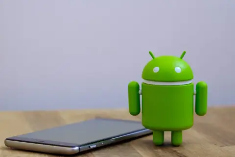 Zielony robot Android obok telefonu, gotowy na aktualizację do android 14.