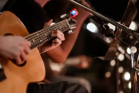 Ręce grające na gitarze akustycznej, w tle migoczą światła, tworząc atmosferę jak na stena line dyskotece.