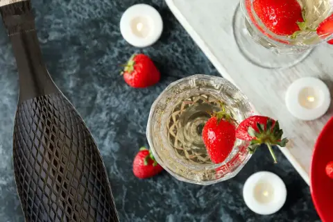 Butelka i kieliszki pełne musującego prosecco, ozdobione truskawkami i świecami. Idealne na romantyczny wieczór.
