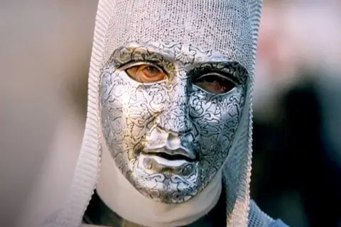 En mystisk figur med en detaljerad silvermask och kedjehätta, en karaktär från rollistan i Kingdom of Heaven.