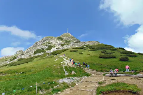 Tłum ludzi wspina się po kamienistym szlaku na Giewont. Widać krzyż na szczycie.