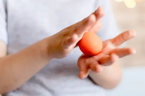 Dłonie trzymają pomarańczowe jajko, które może posłużyć jako naturalny kosmetyk do pielęgnacji włosów.
