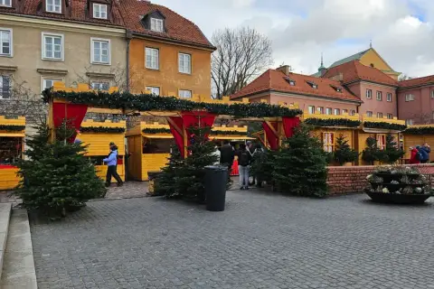 Jarmark świąteczny Warszawa: drewniane budki ozdobione choinkami i lampkami, ludzie spacerują wśród świątecznych dekoracji.