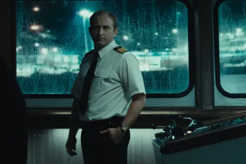 Kapitan w białej koszuli i krawacie stoi przy sterach statku. Scena z jednego z filmów Jana Holoubka.