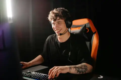 Uśmiechnięty gracz w słuchawkach siedzi przy komputerze, gotowy do gry. Jeśli zapomniałeś hasła, dowiedz się, jak zresetować hasło na Steam.