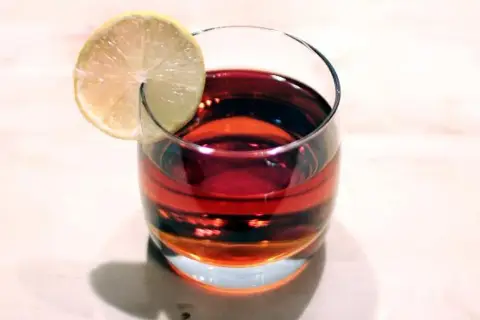 Szklanka z ciemnoczerwonym Martini Rosso, ozdobiona plasterkiem cytryny, stoi na jasnym blacie.
