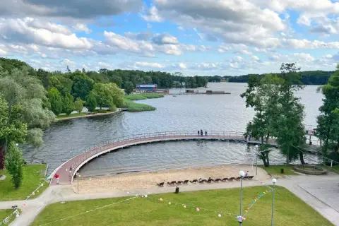 Malownicze jezioro w Szczecinku z łukowatym mostkiem, piaszczystą plażą i zielonymi terenami rekreacyjnymi.