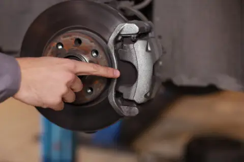 A mechanic's finger points to the dot brake pad thickness, indicating it's time for a replacement.