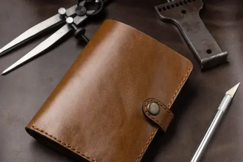 Brązowy portfel ze skóry, narzędzia do obróbki skóry: cyrkiel, dziurkacz, nożyk. Leather cuir to znaczy skóra.