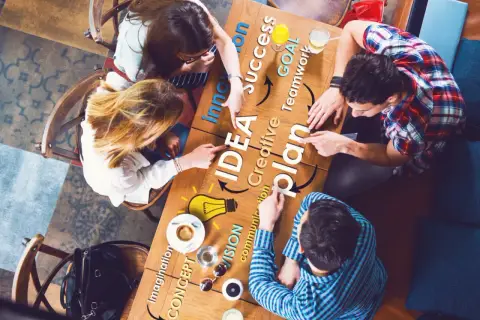 Zespół przy stole dyskutuje nad planem, rozwijając swoją kreatywność. Słowa "IDEA", "plan", "success" i "goal" tworzą mapę myśli.