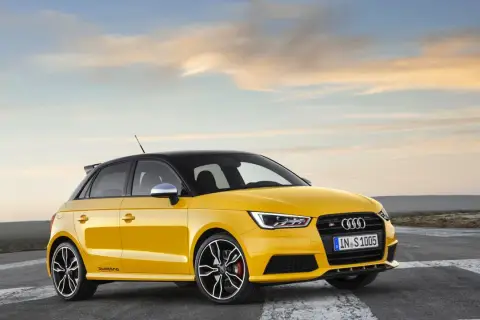 Żółty Audi RS1 z czarnym dachem i felgami, gotowy do jazdy po pustej drodze o zachodzie słońca.
